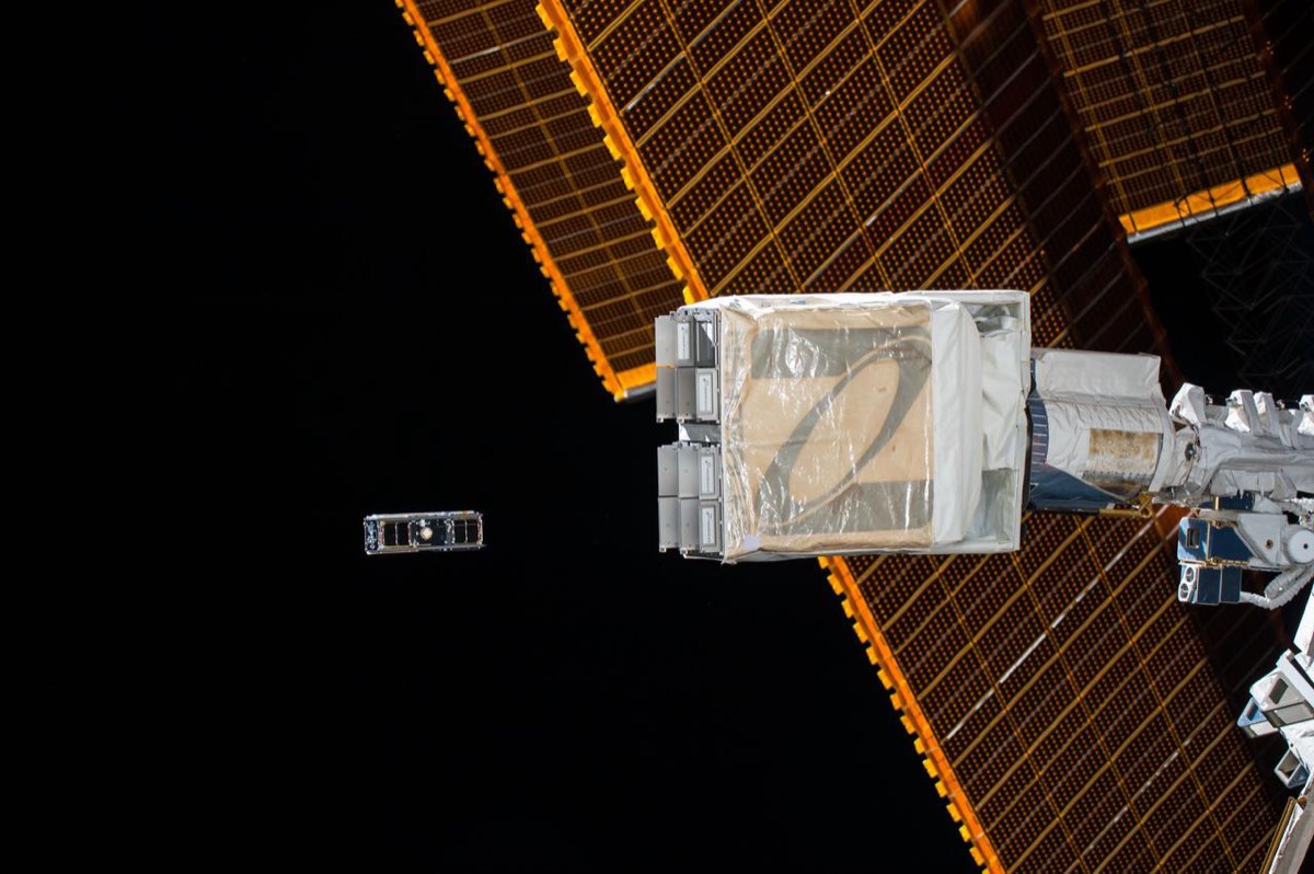 Un CubeSat recién liberado de su dispensador flota contra el negro del espacio, junto a un panel solar de la estación.