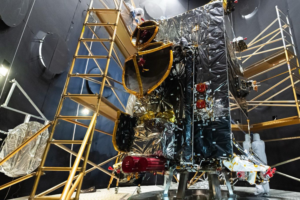 Satélite envuelto en aislante multicapa, rodeado de andamios dentro de una gran cámara de termovacío.