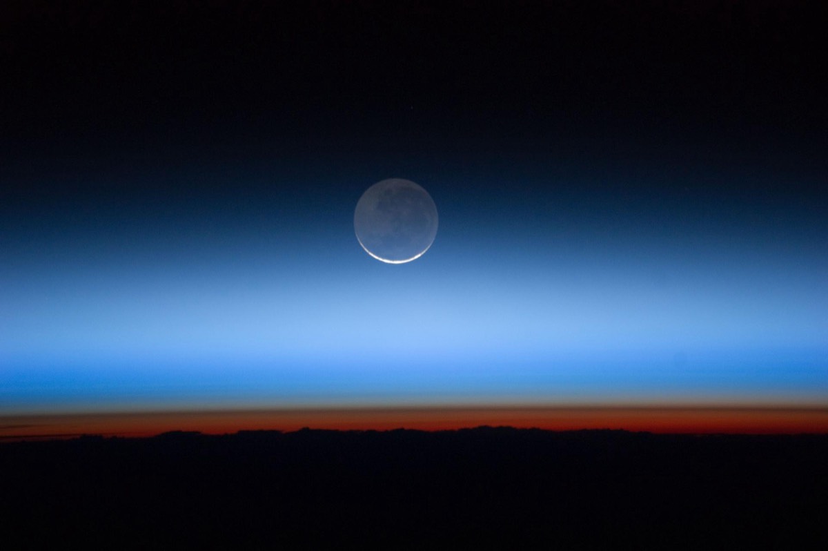 Las capas de la atmósfera en el terminador, de naranja a azul intenso, con la Luna creciente encima, fotografiadas desde la Estación Espacial Internacional.